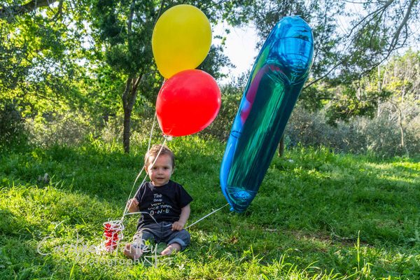 Baby with balloons for his birthday sitting in field